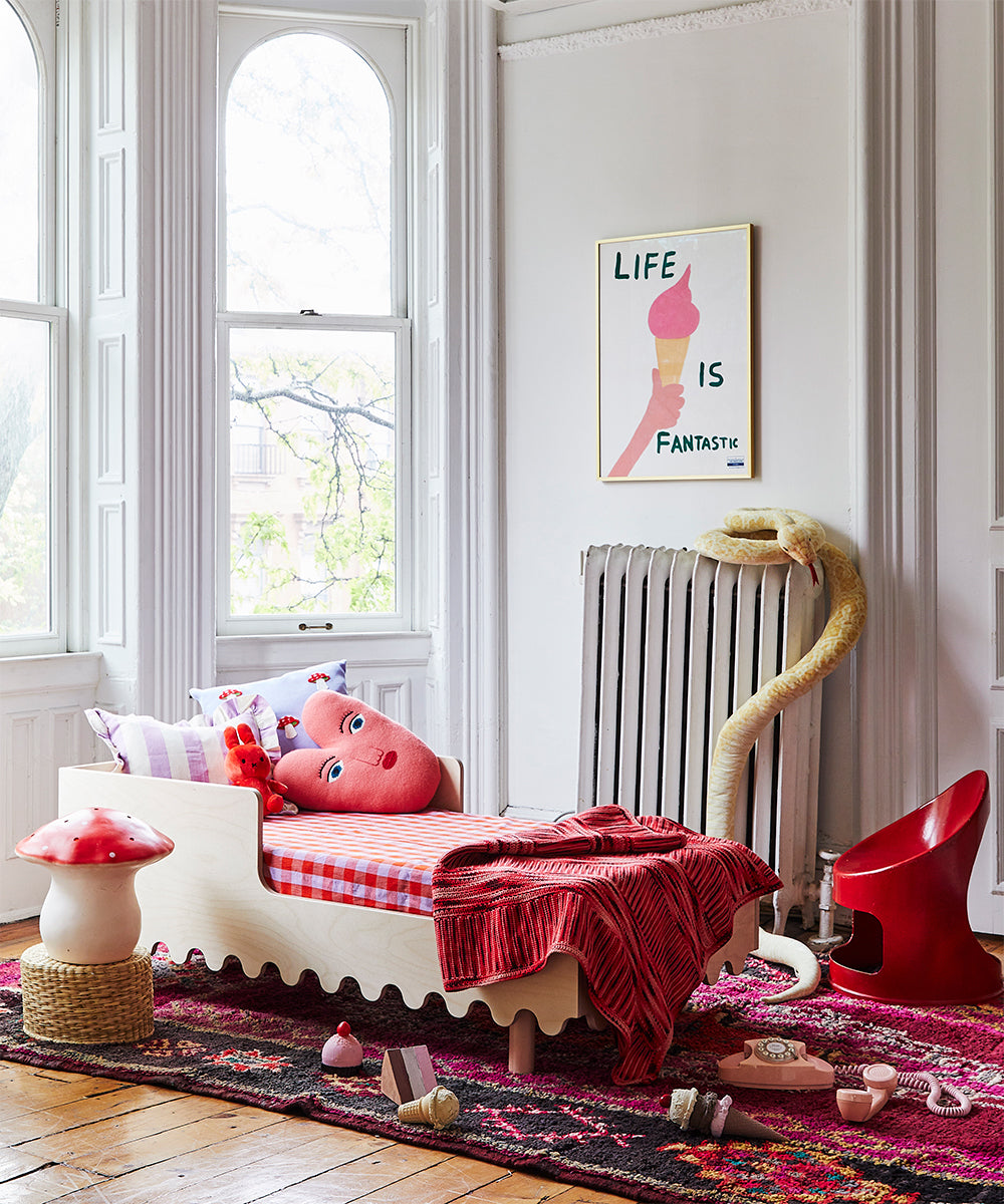 Cozy childs room with a Moss Toddler Bed, red blanket, plush toys, artwork, and a red chair by large windows.