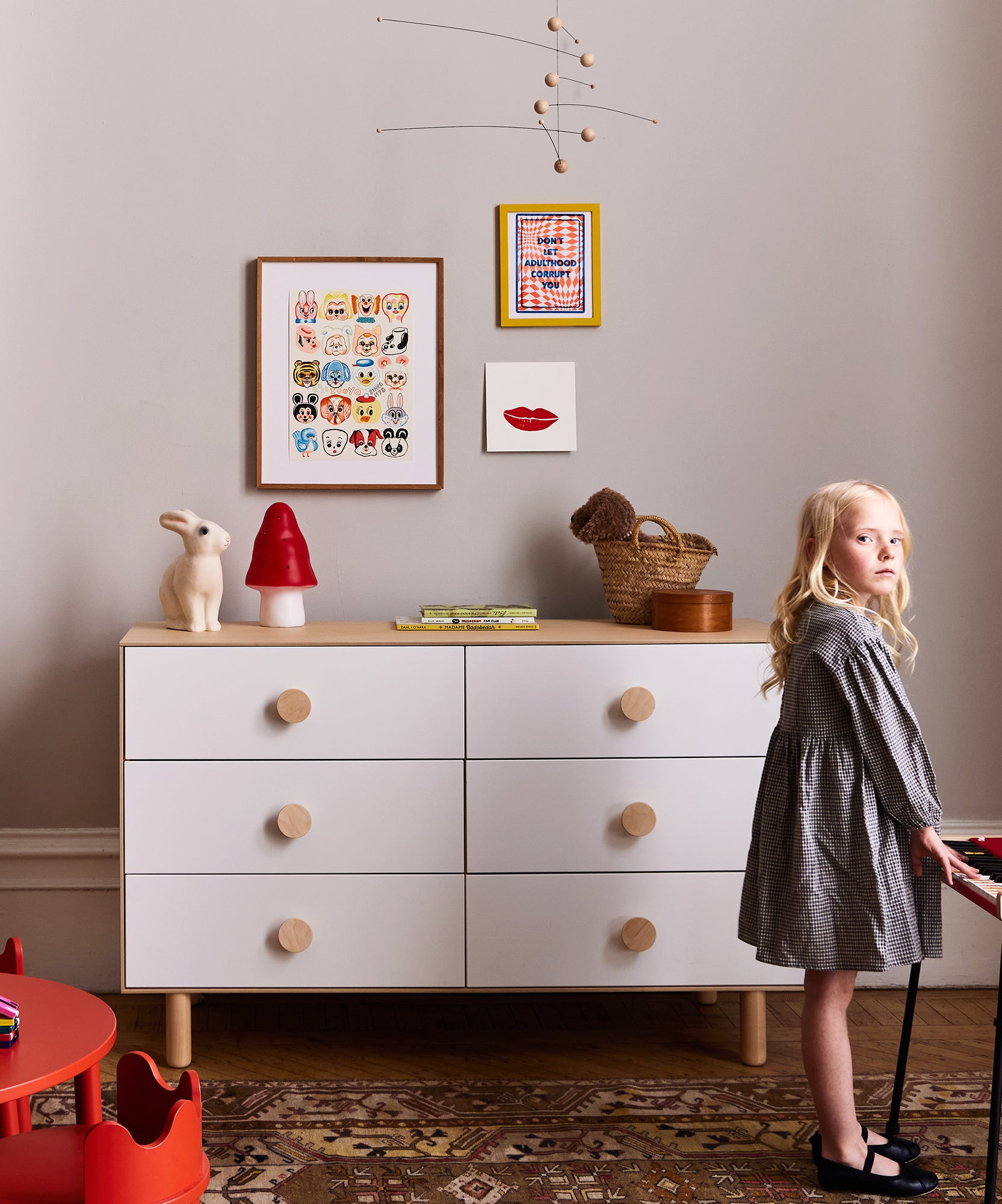 A young girl stands by the Dot 6-Drawer Dresser in a cozy, decorated children's room featuring wall art and toys.