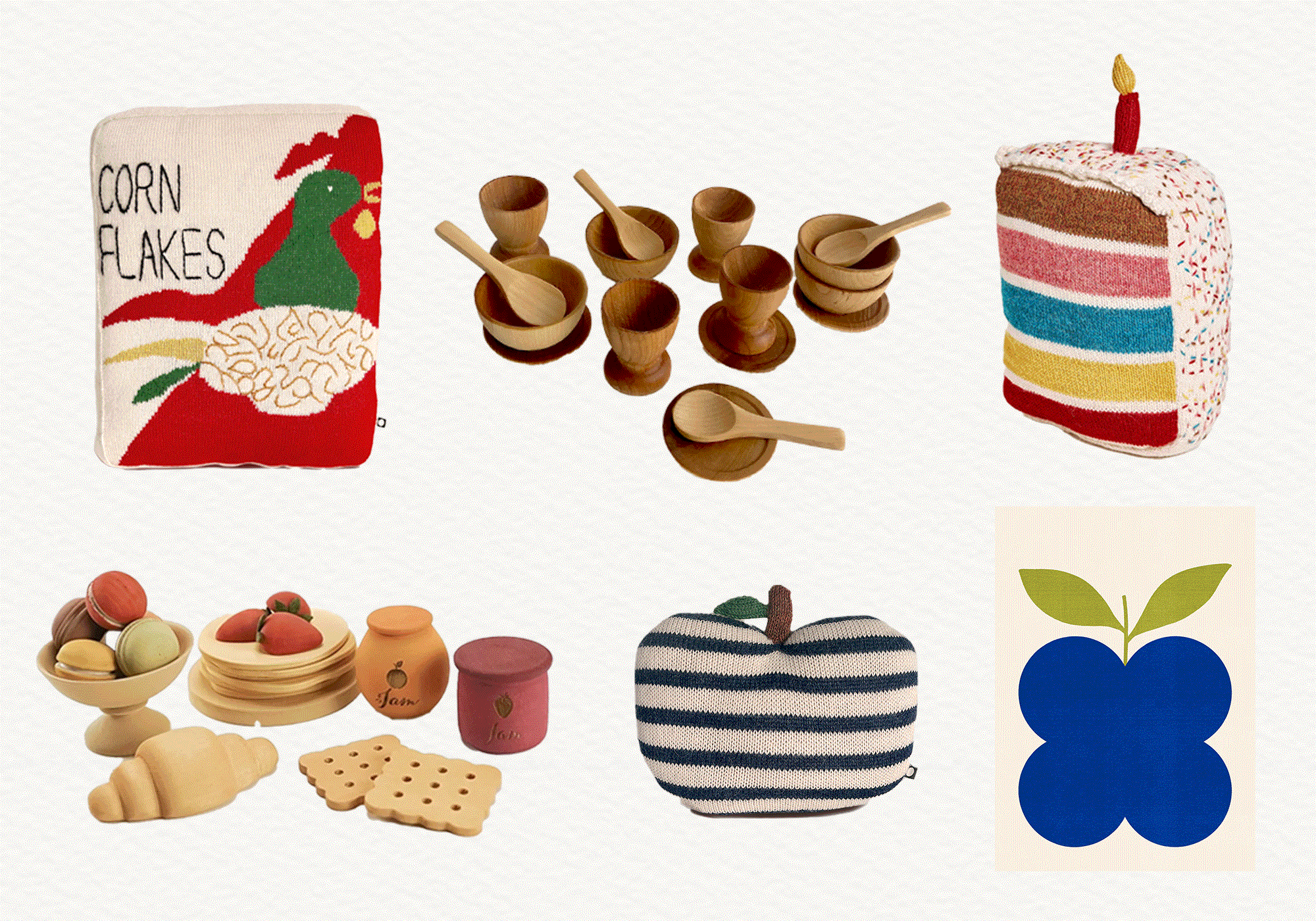 Collection of toy objects: a Corn Flakes pillow, wooden bowls with spoons, cake slice, play food set, jam jars, striped apple pillow, and blue apple print on a white background.