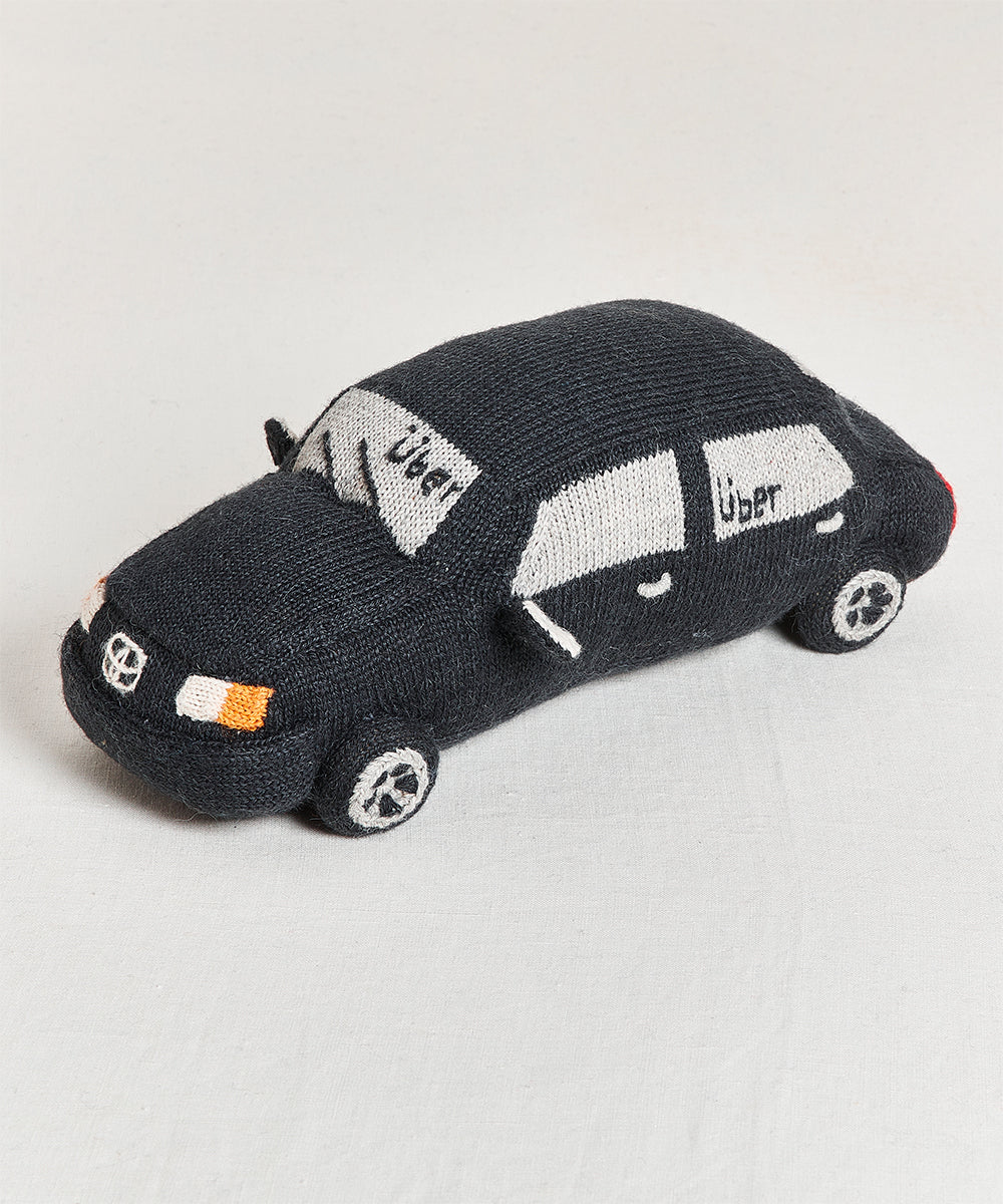 The My Ride Pillow is a knitted black toy car with "Uber" on the side windows, resting on a light surface.