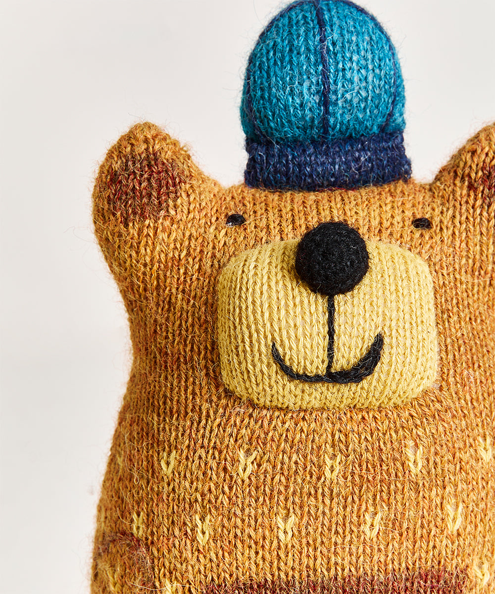 Honey Bear Pillow featuring a smiling knitted bear plush in a blue hat on a plain white background.