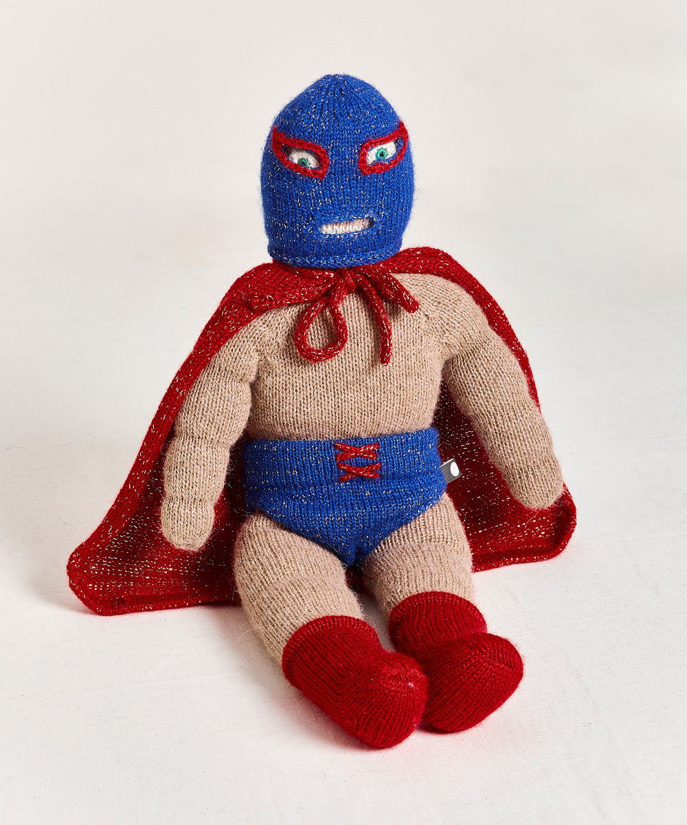 The Wrestler Doll, featuring a blue mask, red cape, blue shorts, and red boots, is seated against a white background.