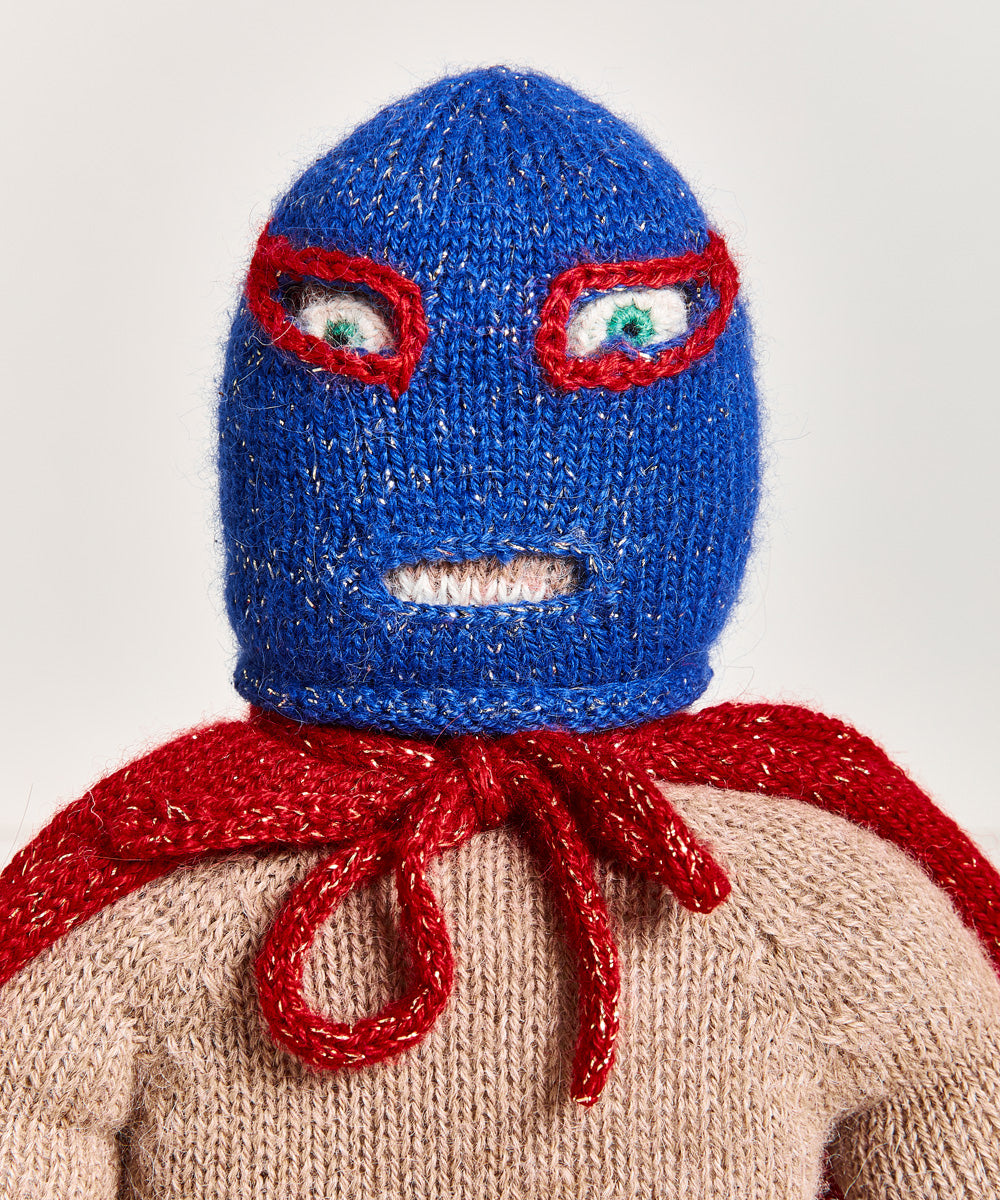 A Wrestler Doll, dressed in a blue mask and red cape, stands against a plain background.