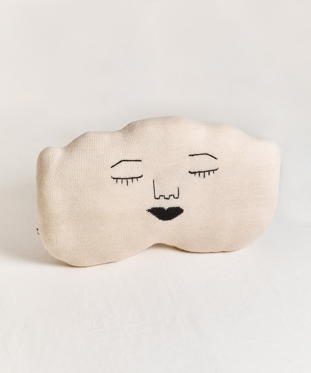 The Cloud Pillow is cream-colored and cloud-shaped with a minimalist face design featuring closed eyes and a black heart-shaped mouth.